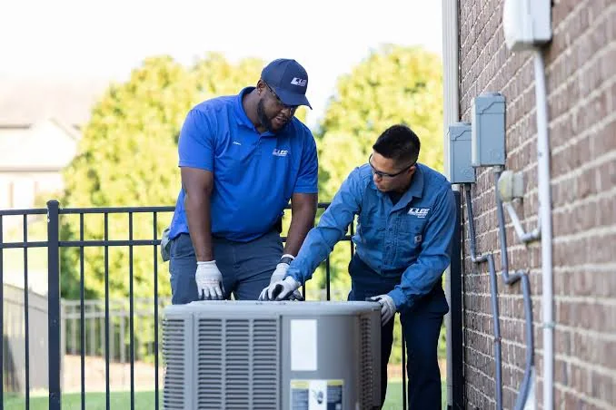 Two HVAC technicians installing an outdoor air conditioning unit beside a home
