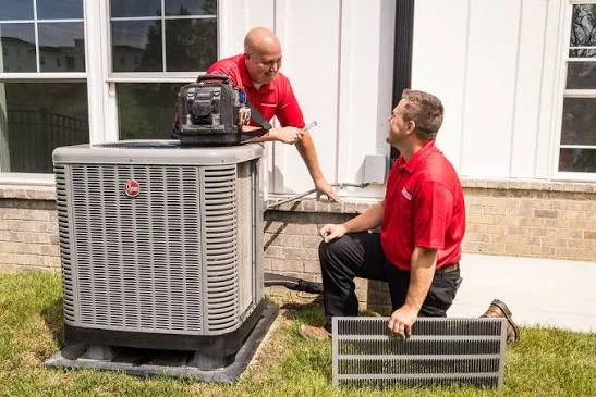 Two HVAC technicians inspecting an outdoor home air conditioning unit